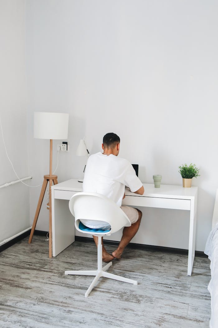 Adult male sitting at a desk studying online in a bright, minimalist room.